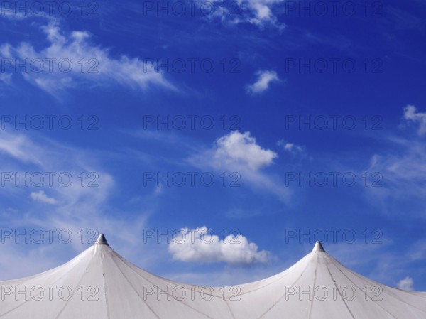 Exhibition tent under a bright blue sky adorned with fluffy clouds in a lively outdoor setting