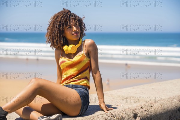 Young woman with headphones relaxing on beach wall enjoying summer vacation, looking away from camera
