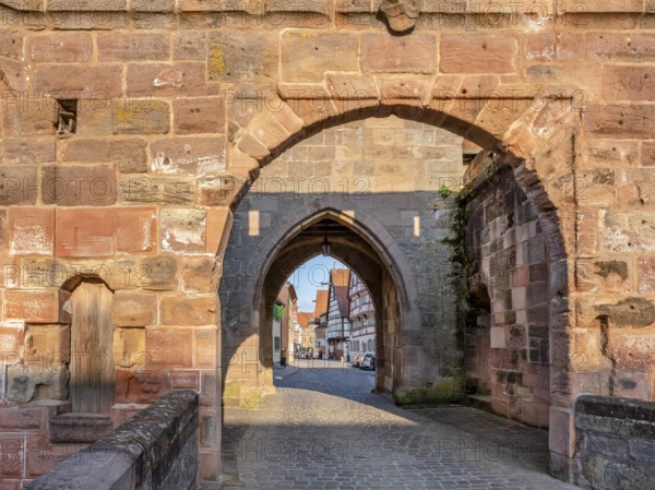 Alley with cobblestones leads through the town gate Oberes Tor, view through the gate to the half-timbered houses of the old town in the evening light, Wolframs-Eschenbach, Middle Franconia, Bavaria, Germany