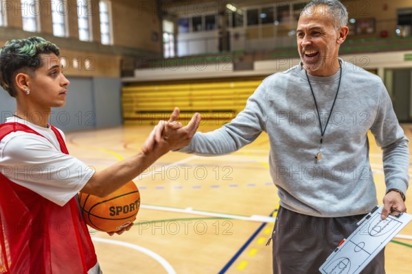 Basketball coach explaining game strategy using clipboard to young player holding ball in a gymnasium