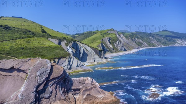 Breathtaking aerial view of the iconic zumaia flysch cliffs meeting the vibrant turquoise waters of the bay of biscay on a sunny summer day, Spain.
