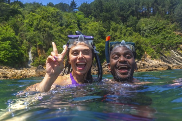 Young multi ethnic couple enjoying snorkeling together in crystal clear tropical sea, woman making victory sign