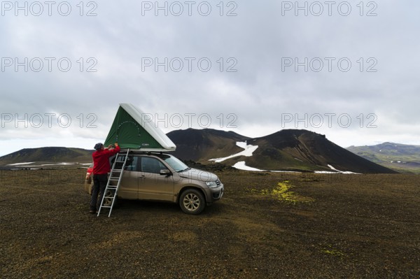 Barren volcanic landscape with snowfields, off-road vehicle with roof tent and ladder on mountain peak, camping, rain clouds, Snaefellsjökull, Snæfellsnes peninsula, Snaefellsnes, West Iceland, Iceland