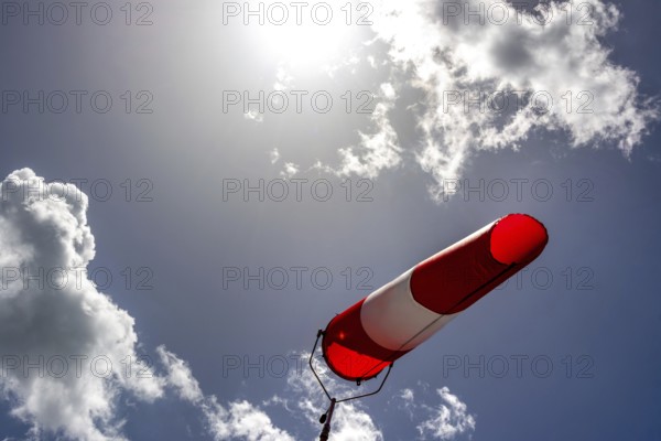 A colorful windsock hangs from a tall pole, clearly indicating wind direction. The bright sky is filled with scattered clouds, creating a vivid backdrop during daytime