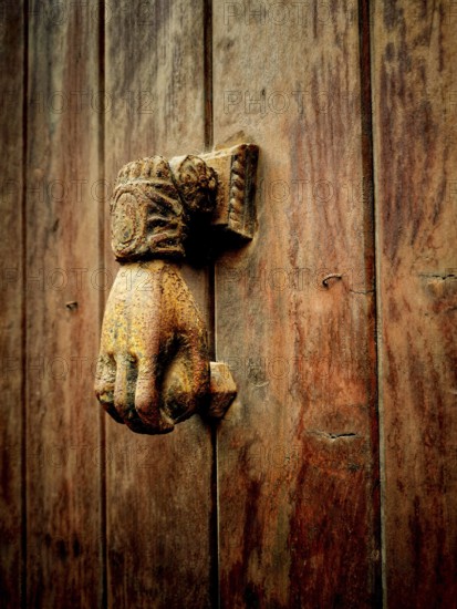 A vintage hand-shaped door knocker is mounted on a weathered wooden door, showcasing intricate designs and a rich patina, adding charm and character to the entrance
