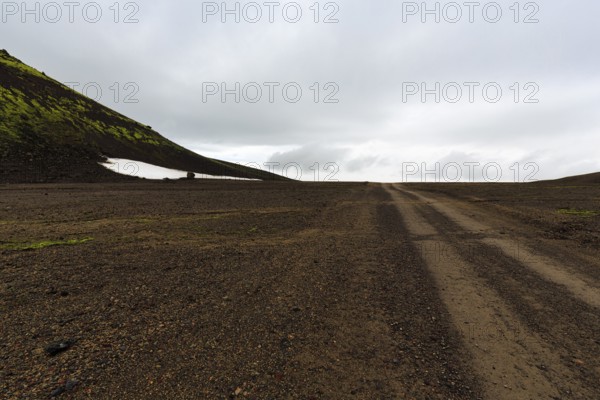 Gravel track, barren volcanic landscape with snowfields, mountain peaks with rain clouds, Snaefellsjökull, Snæfellsnes peninsula, Snaefellsnes, West Iceland, Iceland