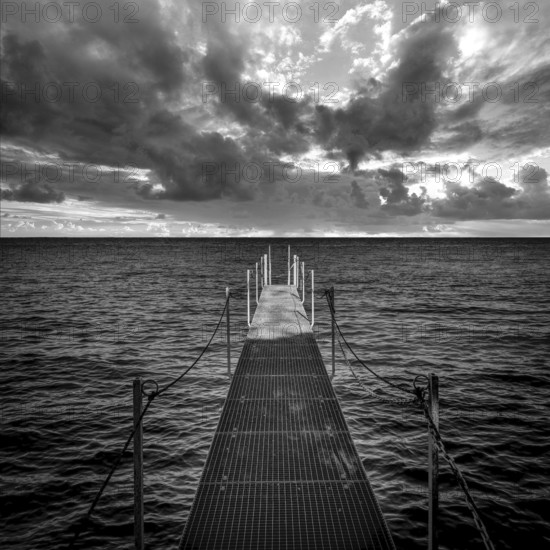 A serene jetty stretches over the calm waters of Lake Geneva, surrounded by dramatic skies filled with clouds. Visitors can enjoy a peaceful atmosphere while taking in the tranquil lake views. Haute Savoie. Auvergne Rhone Alpes. France