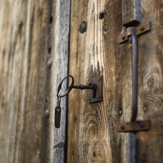 Close-up view of a rustic wooden door featuring a vintage lock and key. The texture of the wood and metal gives a classic charm, highlighting craftsmanship and history. Auvergne. France