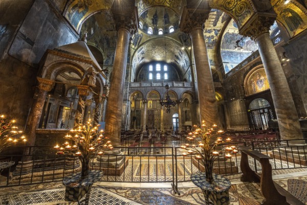 Lit candelabras illuminate the mosaic decorations and marble columns inside saint mark's basilica in venice, italy