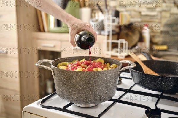 A person pours red wine into a pot filled with pork and vegetables making aromatic sauce