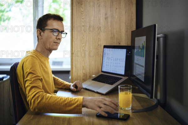 A man in a yellow shirt sits at a desk in a home office. He was distracted from studying statistics by a phone call