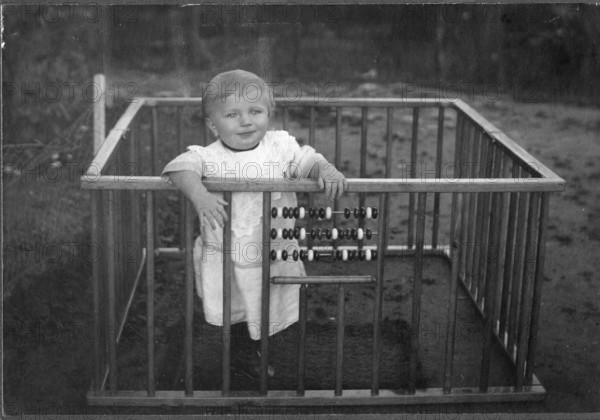 Child in a playpen, 1920s, A smiling child stands in a grid with an abacus in a nostalgic, historical setting, Historical photo