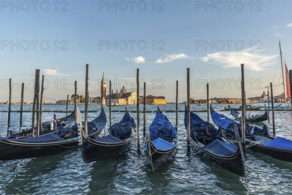 Gondolas moored at sunset with the island of san giorgio maggiore in the background, creating a picturesque venetian scene