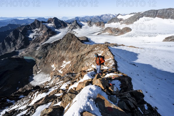 Mountaineer on a rocky ridge on the Wilder Freiger summit, behind him Signal summit and Becher summit with Becherhaus, picturesque high mountain landscape, view of Übeltalferner glacier and rocky mountain peaks Königshofspitz and Sonklarspitze, Stubai Alps, South Tyrol, Italy