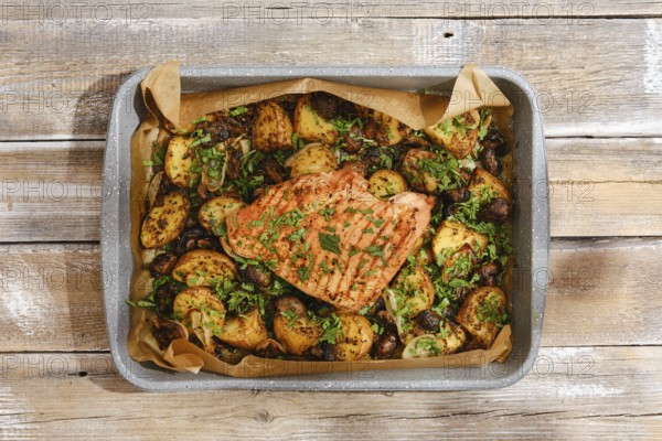 A roasted turkey breast rests atop a bed of golden, seasoned potatoes, vibrant herbs sprinkled over. The rustic wooden table enhances the warm and inviting atmosphere for a savory meal