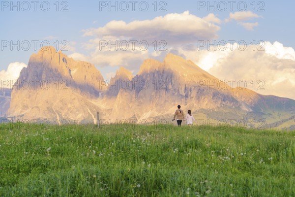 Couple in a meadow in front of picturesque mountains at sunset, Alpe di Siusi, Dolomites, South Tyrol, Italy
