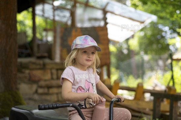 Girl, 3 years, blonde, sitting on bicycle in the garden, summer, Stuttgart, Baden-Württemberg, Germany