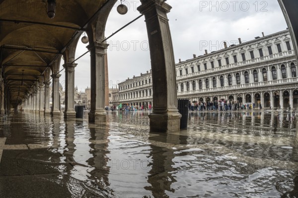 Tourists visiting piazza san marco in venice, italy, despite the rain causing flooding under the arches