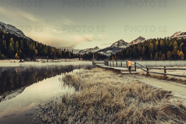Young woman at Lake Staz near Sankt Moritz in the Engadine in Switzerland. Morning atmosphere with fog in autumn. Reflection of water