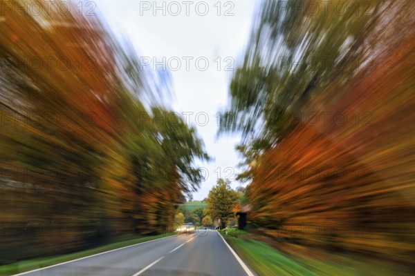Country road through autumn forest, autumn leaves, oncoming traffic, light traces, cloudy weather, zoom effect, motion blur, Solling-Vogler nature park Park, Lower Saxony, Germany