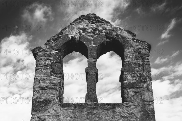 Crumbling stone ruins of a bell tower stand against a cloudy sky, showcasing two arched windows. Puy de Dome. Auvergne Rhone Alpes. France