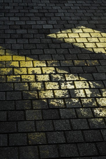 Faded yellow markings on dark, textured stone pavement create a striking contrast. The uneven surface suggests wear and age, showcasing an outdoor environment in low light