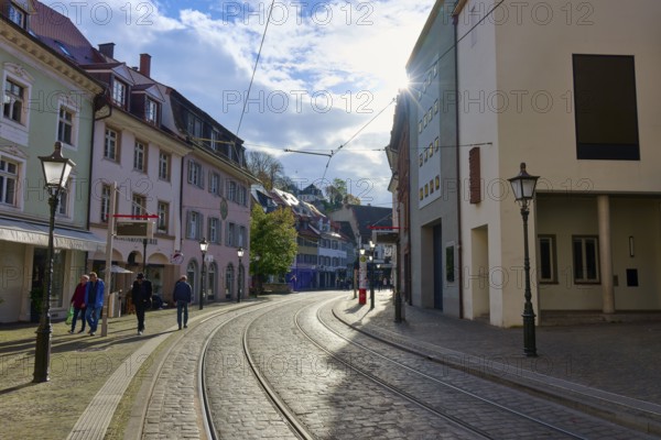 City street with railway tracks, lined with modern buildings and bustling with people, Freiburg im Breisgau, Black Forest, Baden-Württemberg, Germany