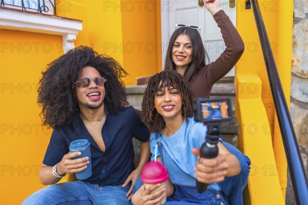 Three happy multi ethnic content creators filming a video blog with a gimbal and drinking smoothies on colorful steps