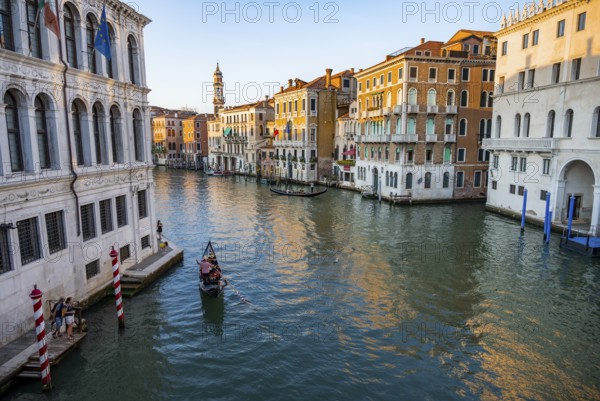View of the Grand Canal with gondoliers at sunset, picturesque evening mood with palazzos on the canal and church tower of the Chiesa Parrocchiale dei Santi Apostoli, view from the Rialto Bridge, Venice, Veneto, Italy