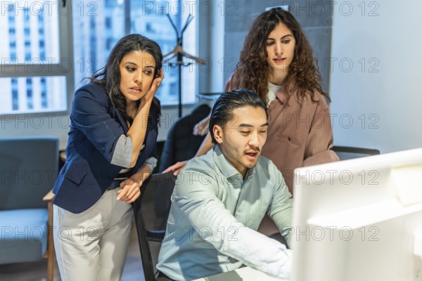Diverse colleagues collaborating on a project, focusing on a computer screen, demonstrating teamwork and problem solving in a professional setting