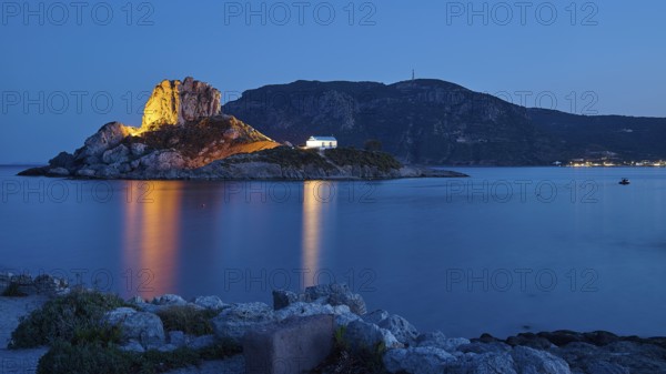 Rocks and buildings on an island, illuminated at night with reflecting water, Agios Stefanos Beach, Agios Stefanos Basilica, Chapel of Agios Nikolaos, Kastri Island, Kos, Dodecanese, Greek Islands, Greece
