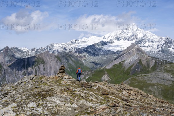 Female mountaineer on hiking trail with cairn, behind glaciated and snow-covered summit of the Großglockner, Wiener Höhenweg, Schober group, Hohe Tauern National Park, Carinthia, Austria