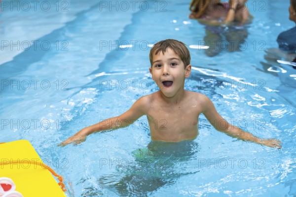 Young boy enjoying his summer vacation, playing and making funny faces in a swimming pool with a yellow kickboard