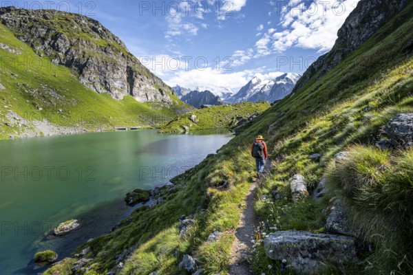 Mountaineer on a hiking trail at a mountain lake with a view of glaciated mountain peaks, Lac du Louvie with summit Grand Combine, Valais Alps, Val de Bagnes, Valais, Switzerland