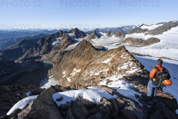 Mountaineer on a rocky ridge on the Wilder Freiger summit, behind him Signal summit and Becher summit with Becherhaus, picturesque high mountain landscape, view of Übeltalferner glacier and rocky mountain peaks Königshofspitz and Sonklarspitze, Stubai Alps, South Tyrol, Italy