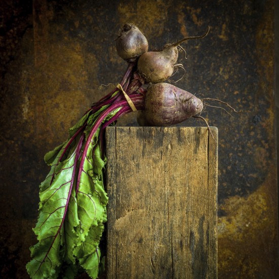 Vibrant red beets with green leaves displayed on rustic wooden surface against textured backdrop