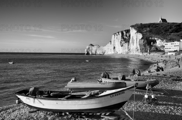 Rowing boat, boats lying on the beach, pebble beach, rock arch Falaise or Porte d'Amont, church Chapelle Notre Dame de la Garde, Étretat, sea, steep coast, cliffs, chalk cliffs, alabaster coast, La Côte d'Albâtre, black and white, Normandy, Seine-Maritime, France
