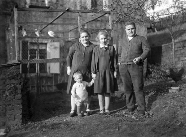 Family in front of a birdcage, 1930s, Family of four standing in a rural garden area, all looking at the camera, Historical photo