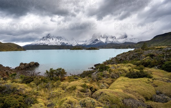 Cloudy mountain range Cuernos del Paine, shore of the blue lake Lago Pehoe in the evening light, dramatic sky, Torres del Paine National Park, Chile