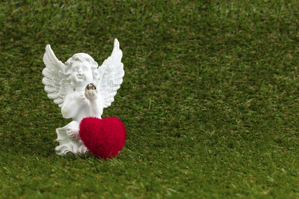 A white angel figure with a red heart on green grass