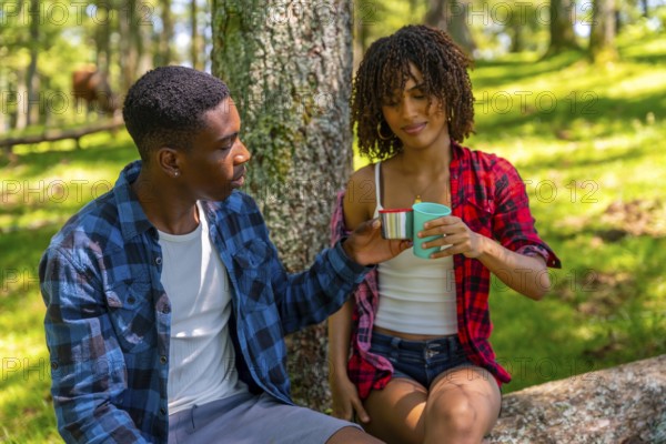 Young couple taking a refreshing break during their hike, sharing drinks from reusable cups while enjoying the serene forest surroundings