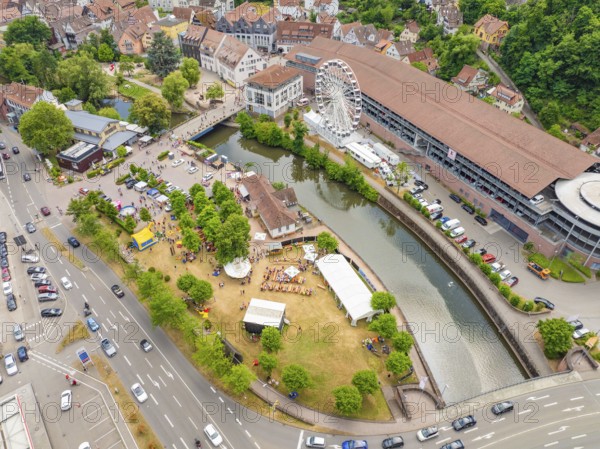 Park with people by a river, flanked by town buildings and a Ferris wheel, with heavy road traffic, 950 years of Calw, Calw parade, Black Forest, Germany