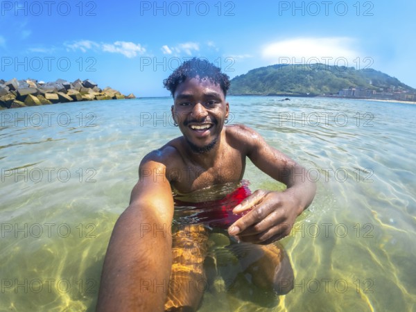Young man enjoying a sunny summer day, capturing a joyful selfie while bathing in crystal clear sea water, surrounded by vibrant nature