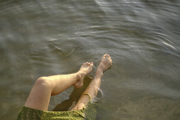 On a sunny day at the lake, a person enjoys the cool water, dipping her feet in while seated comfortably