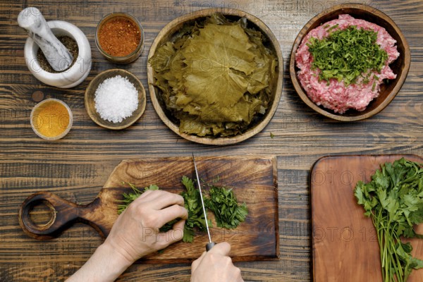Preparing traditional dolma involves chopping herbs and meat, spreading grape leaves, and mixing spices in a cozy kitchen