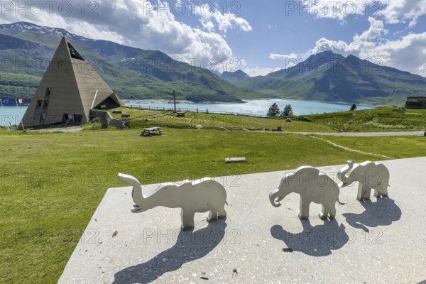 View from viewing platform to Mont-Cenis Pyramid Museum with stylised pyramid Museum in memory of Egypt campaigns of Emperor Napoleon Bonaparte and time in front of construction of reservoir, behind it Lac du Mont Cenis, in front on parapet small stylised figures of elephants Symbols for crossing of Alps Crossing of Alps by Hannibal, Mont Cenis Massif, Massif du Mont-Cenis, Graian Alps, Lanslebourg, Rhone-Alpes, France