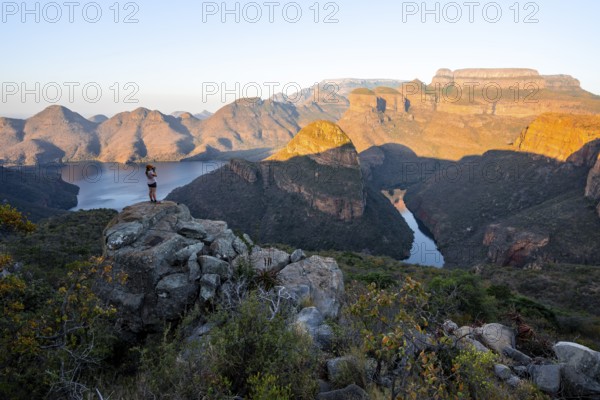 Hiker enjoying sunset at Blyde River Canyon with Three Rondawels peak, view of canyon with Blyde River and table mountains in the evening light, Canyon landscape, Panorama Route, Mpumalanga, South Africa