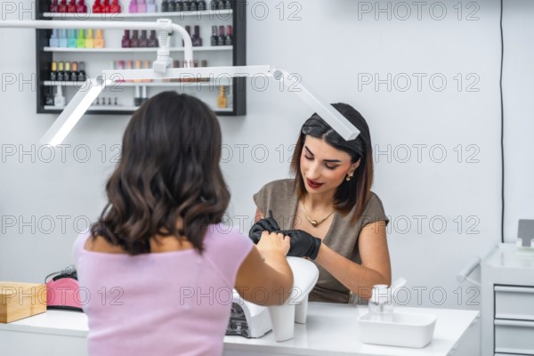 Beautician wearing black gloves carefully applying nail polish on client's nails in a modern beauty salon, creating perfect manicure