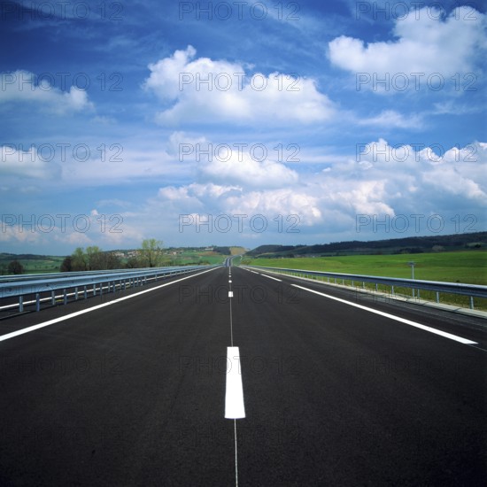 A straight stretch of a French motorway showcases smooth asphalt and clear lane markings. Lush green fields and rolling hills frame the road, creating a peaceful landscape. France