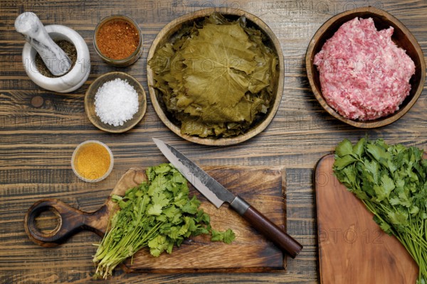 Preparing dolma by assembling marinated grape leaves, ground meat, and herbs on a wooden countertop. Various spices and seasonings are arranged neatly, highlighting a home-cooking atmosphere
